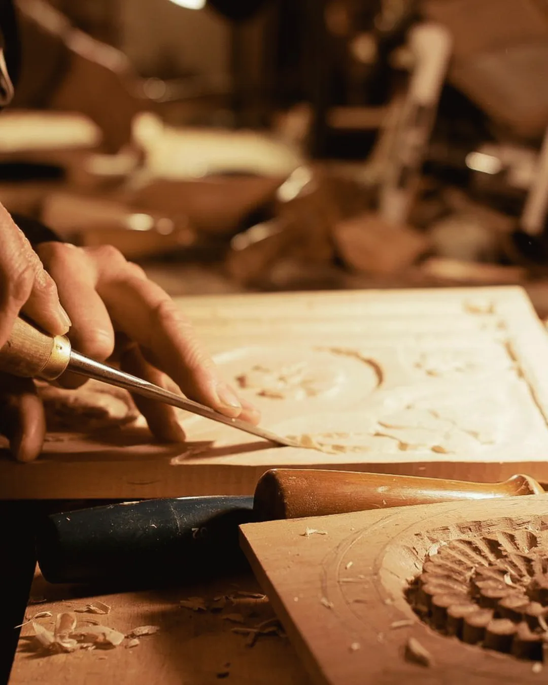 Manos de un artesano tallando un relieve en madera, luz cálida de taller